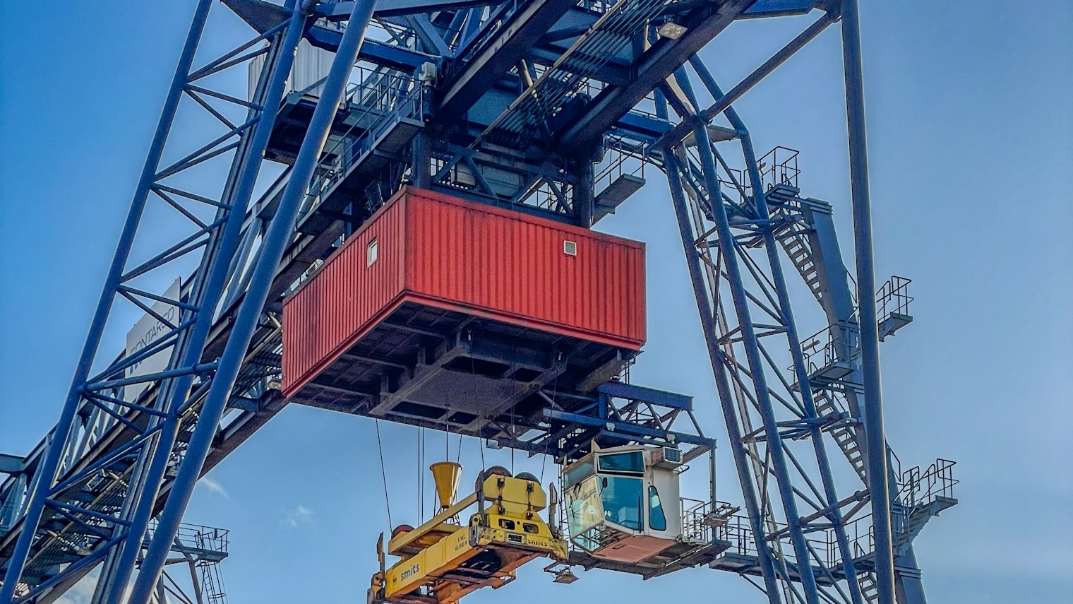 A gantry crane lifting a red container at a terminal