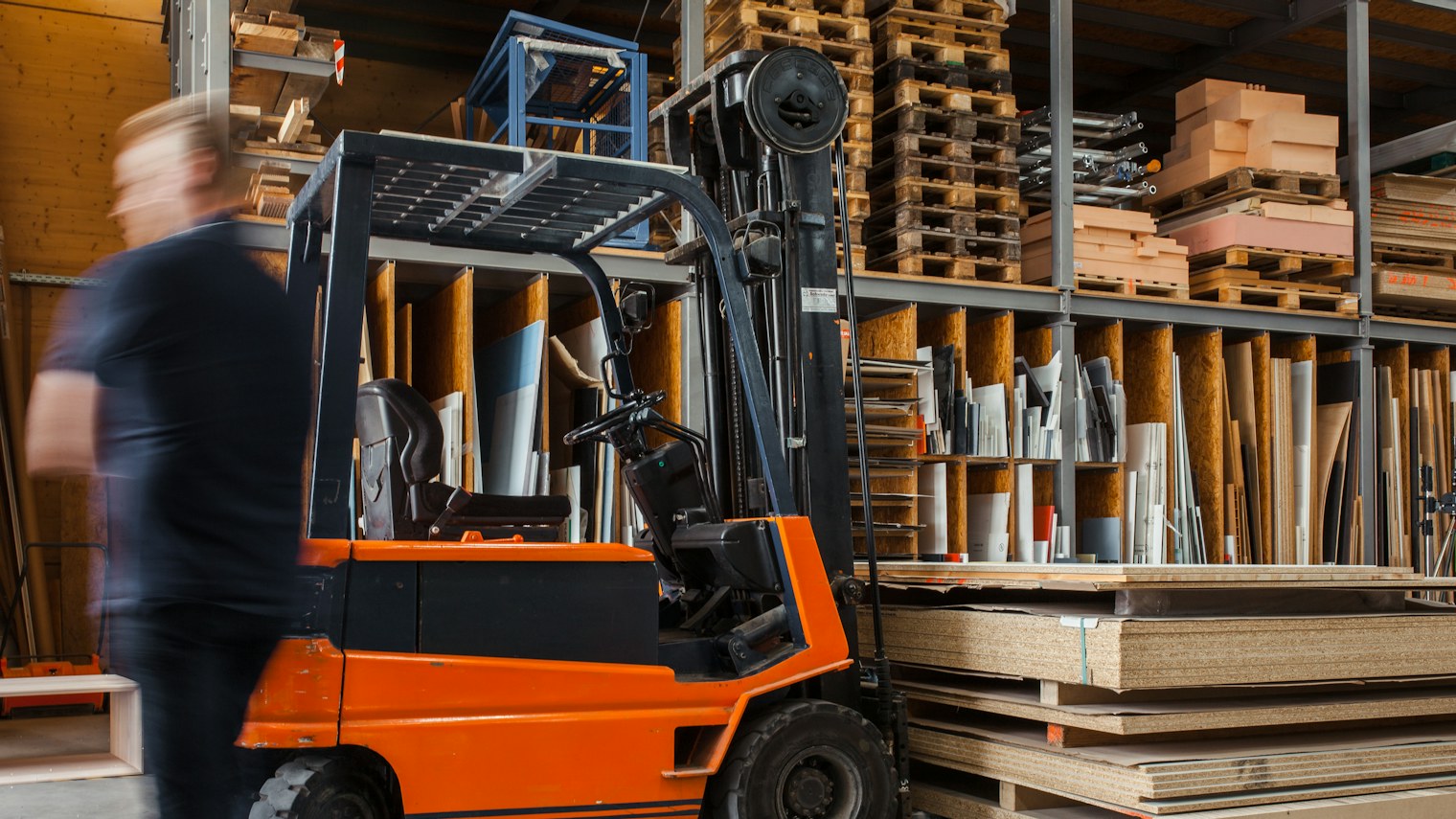 A forklift in a warehouse with wood panels and pallets